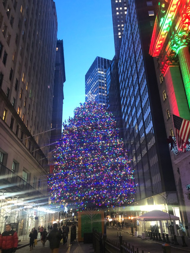 A large decorated Christmas tree with a menorah in front of it in early evening outside the New York Stock Exchange.